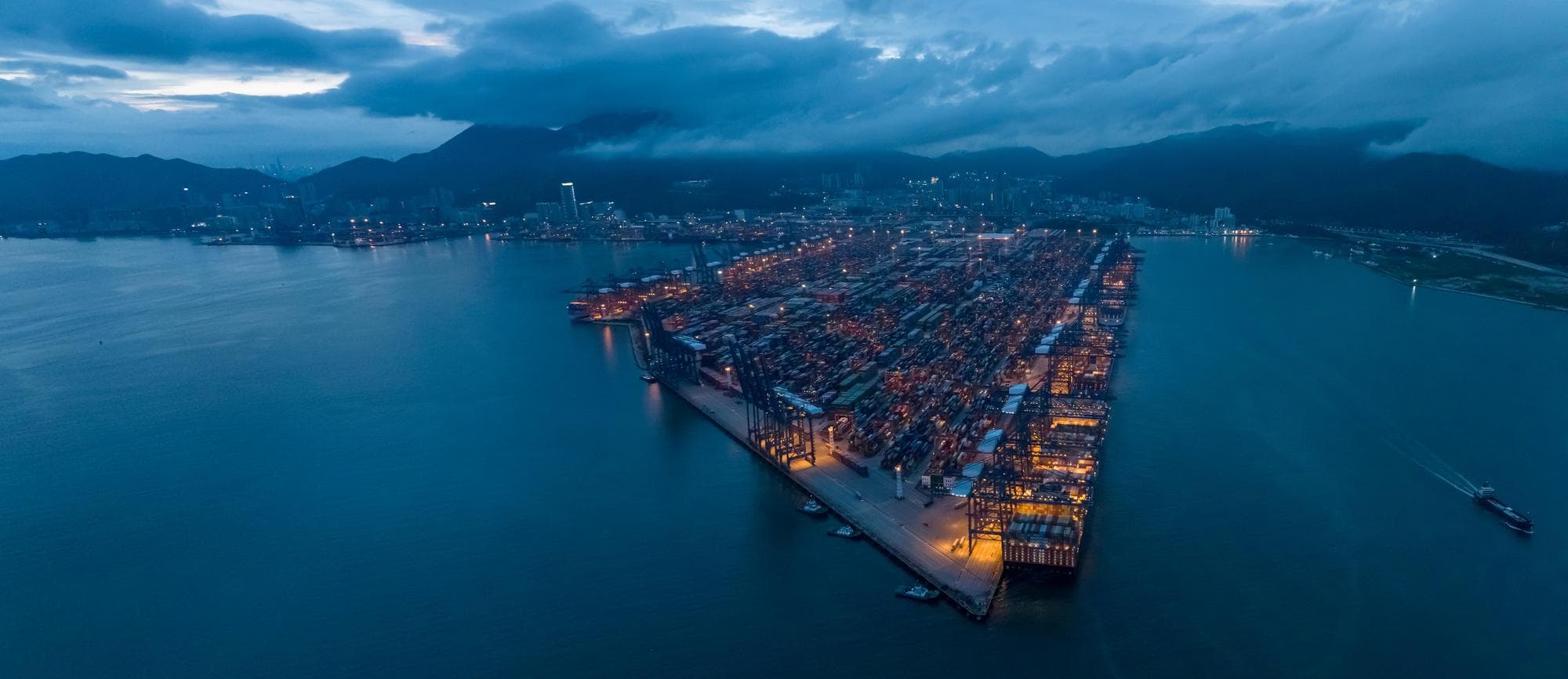 Aerial container terminal at night — global polymer logistics stranded during 2026 Hormuz 275-day resin crisis